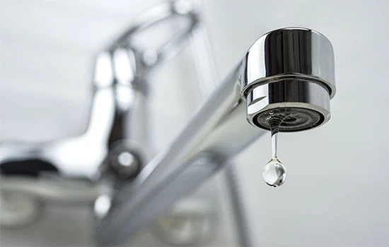 Close-up of a chrome kitchen faucet aerator with a water droplet falling, sink blurred in background
