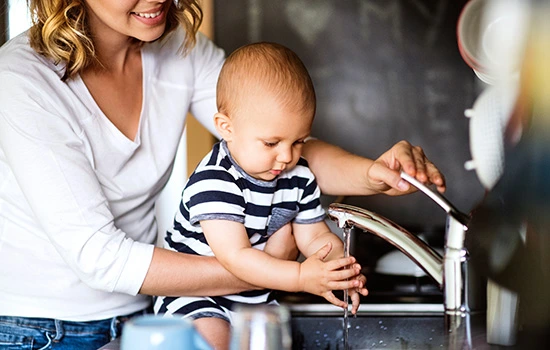 Mother and baby boy washing hands together at kitchen sink, teaching hygiene and cleanliness