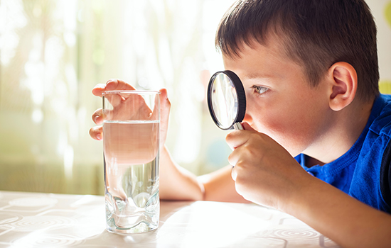 child inspecting a glass of water with a magnifying glass